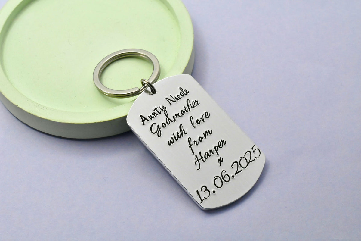 A silver metal dog tag keyring , personalised with with godparent and god childs name, with christening date at bottom.