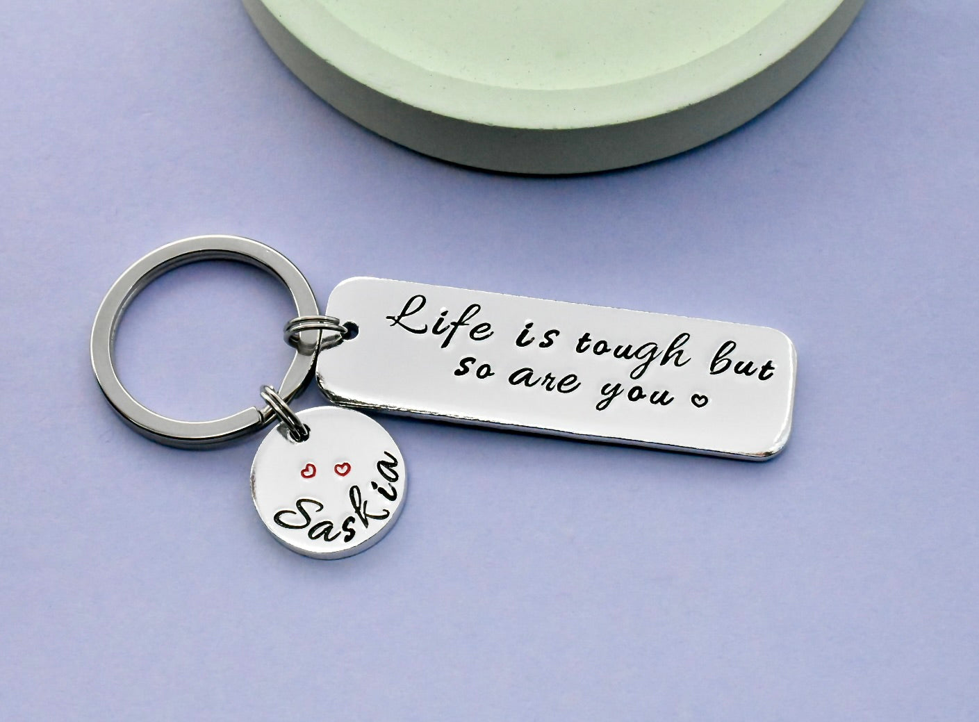 Silver keychain with motivational tag sayimng life is tough but so are you and personalised name charm on a purple background