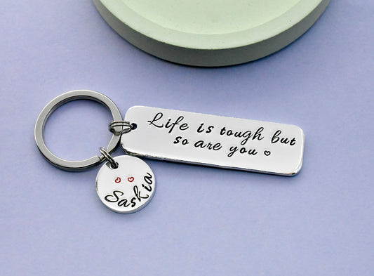 Silver keychain with motivational tag sayimng life is tough but so are you and personalised name charm on a purple background
