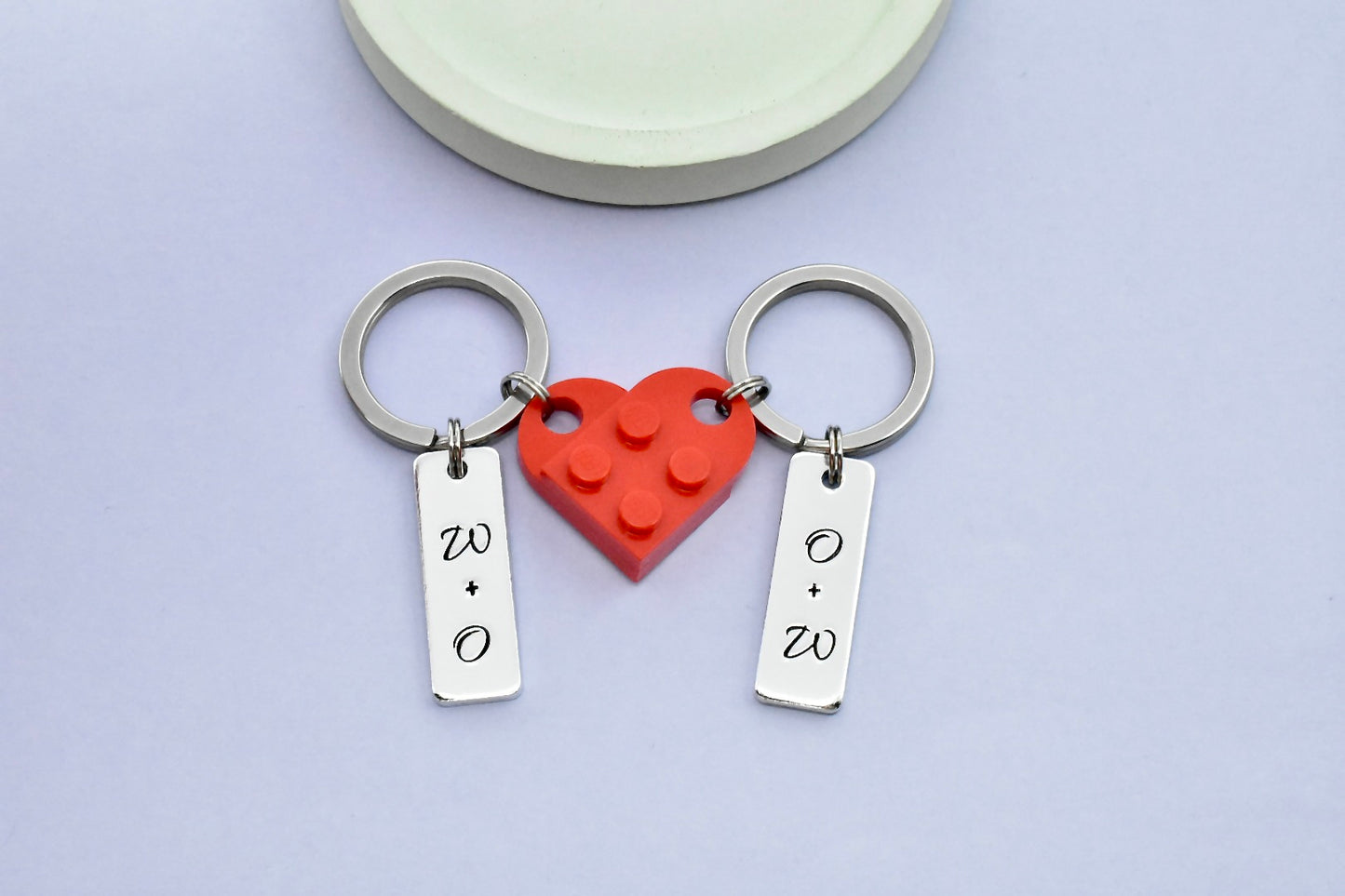 A set of heart-shaped connectable keyrings made of red plastic building blocks, each half of the heart has a small silver aluminium rectangle charm, personalised with couple's initials on each piece 