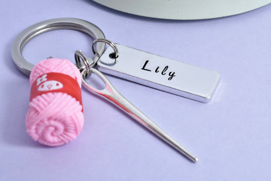 A personalised aluminium keyring with a pink wool charm and a needle charm, featuring the name 'Lily' on a silver name plate.