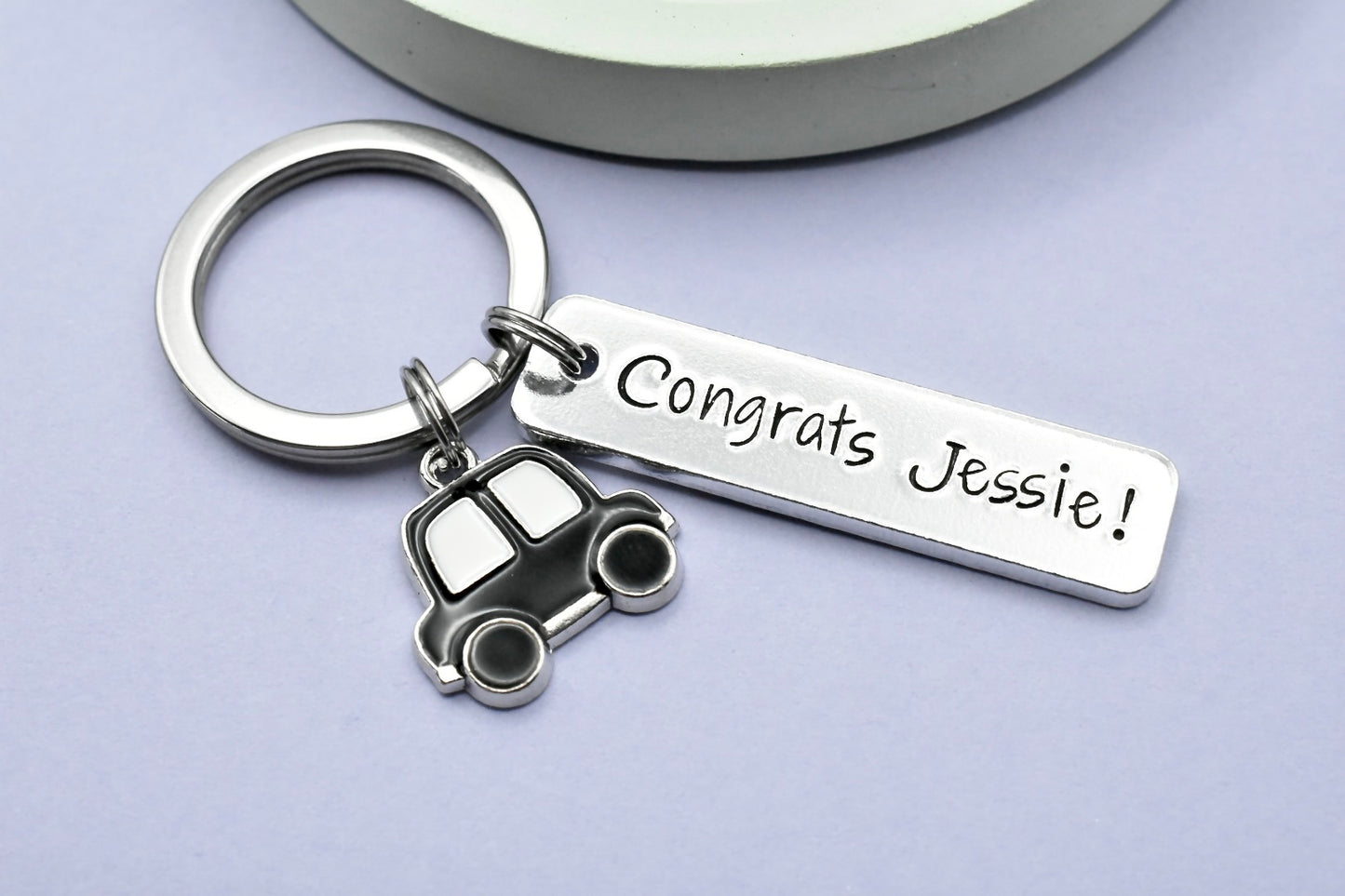 A personalised aluminium keyring with a car charm, featuring the text 'CONGRATS JESSIE!' and a split ring. The keyring is rectangular and has a shiny metallic finish.