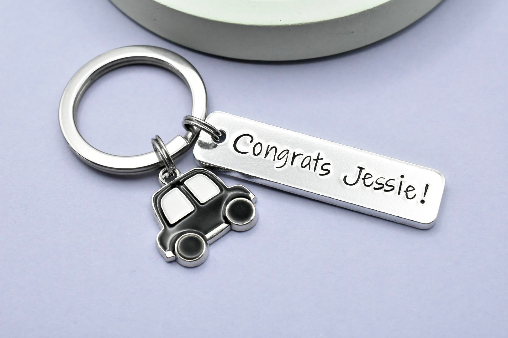 A personalised aluminium keyring with a car charm, featuring the text 'CONGRATS JESSIE!' and a split ring. The keyring is rectangular and has a shiny metallic finish.