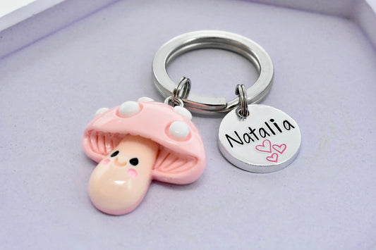 Keychain with a pink mushroom character charm and a round tag with 'Natalia' on a light purple background