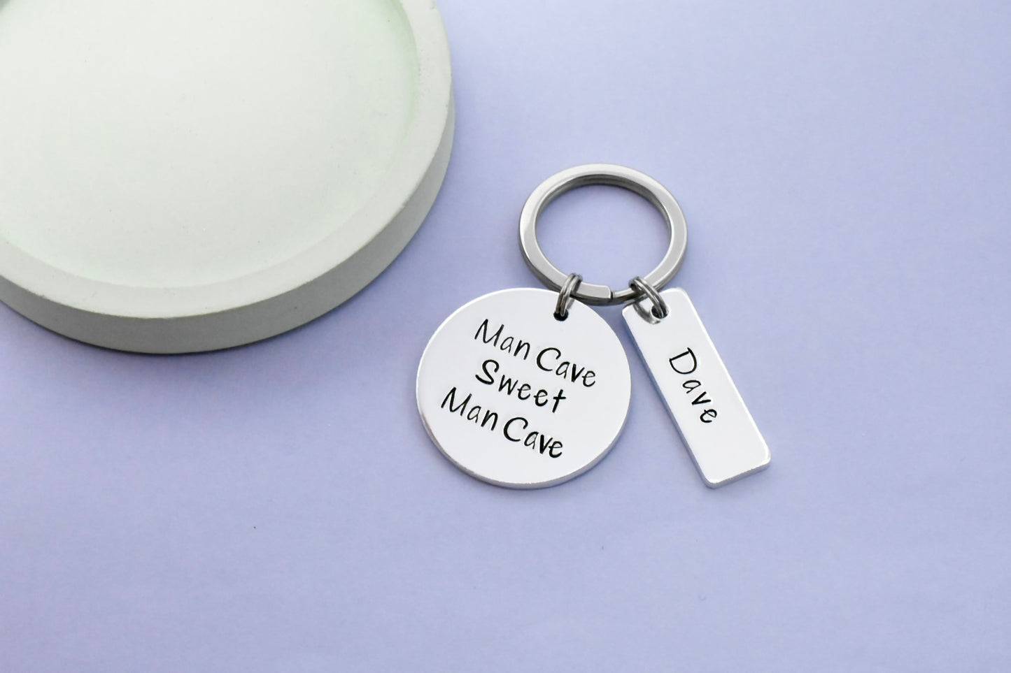 A keyring with a large circular aluminium disc with the text 'Man Cave Sweet Man Cave' and a smaller rectangular tag with the name 'Dave'.