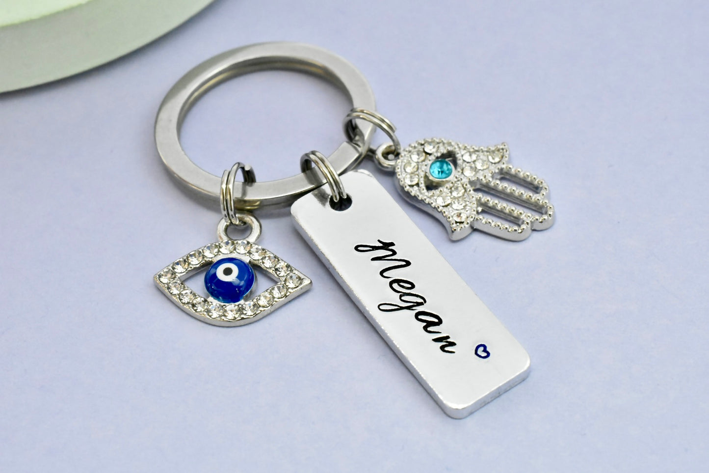 Keychain with Hamsa hand, evil eye, and name tag charm on a light purple background