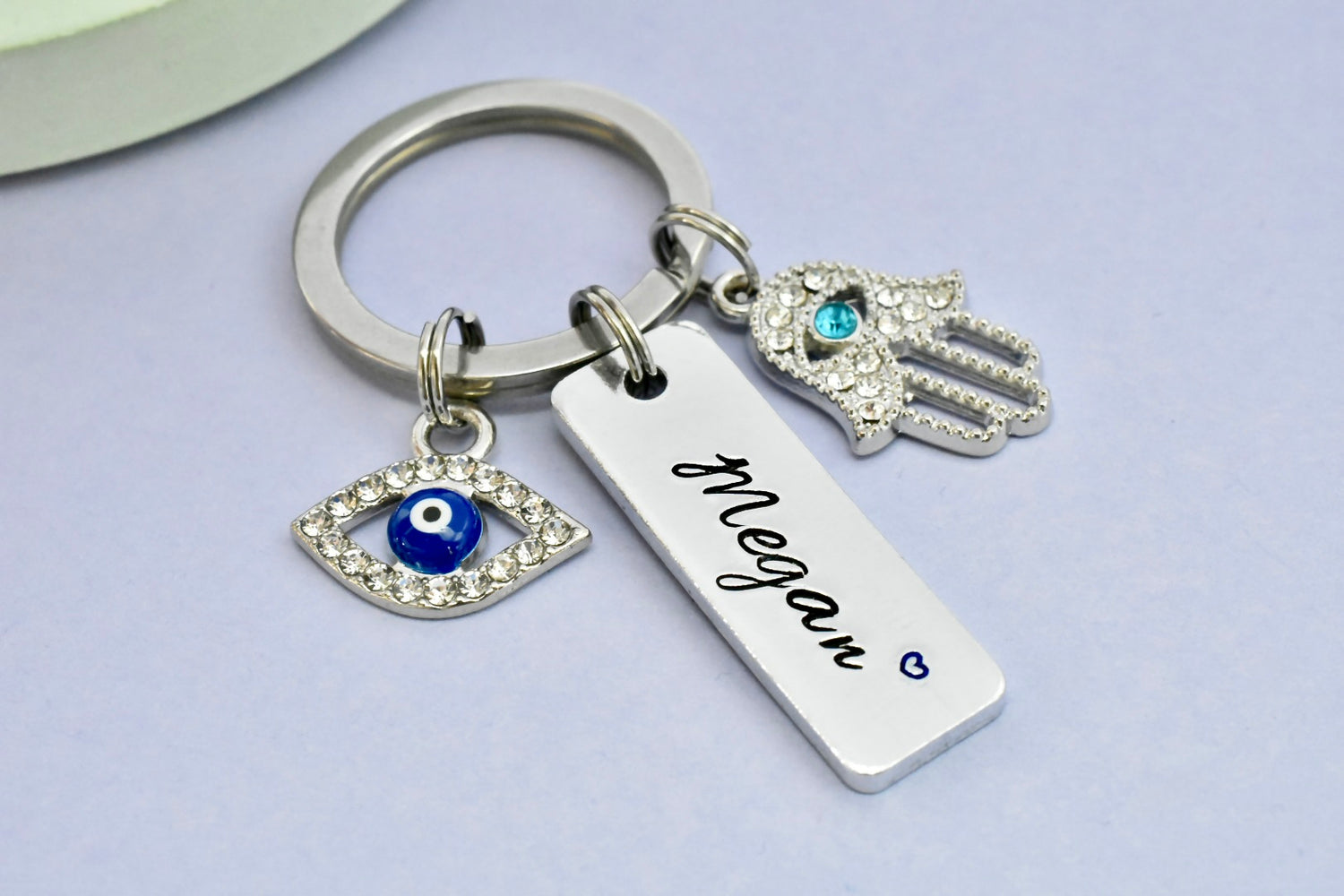 Keychain with Hamsa hand, evil eye, and name tag charm on a light purple background