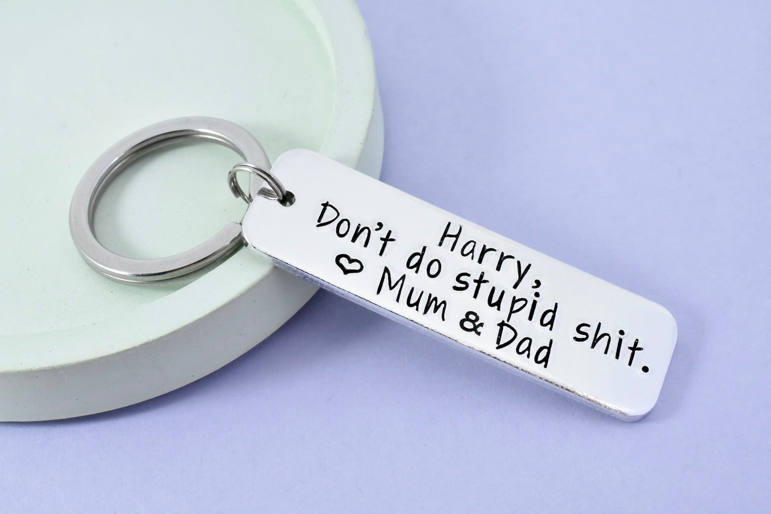 A silver-colored ,personalised keyring with the text 'Harry, Don't do stupid shit' heart symbol and "Mum &Dad" stamped on it, 