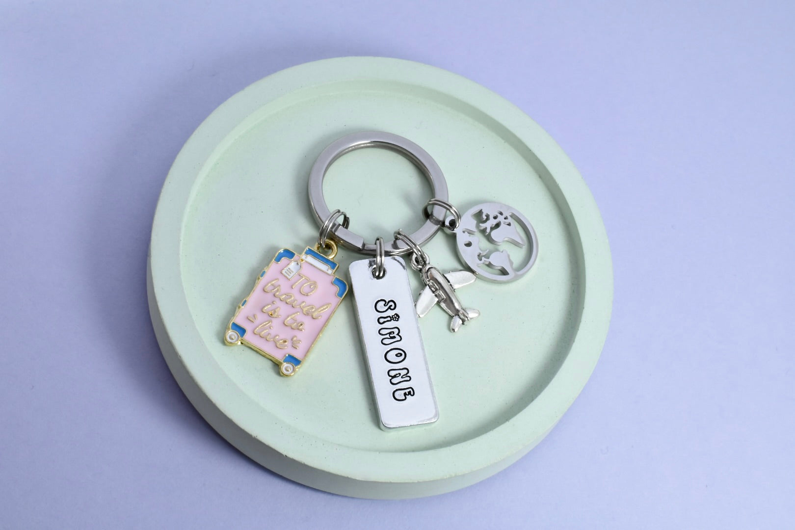 A personalised aluminium keyring with rectangular dimensions, featuring travel-themed charms including a plane, world, suitcase, and a split ring. 