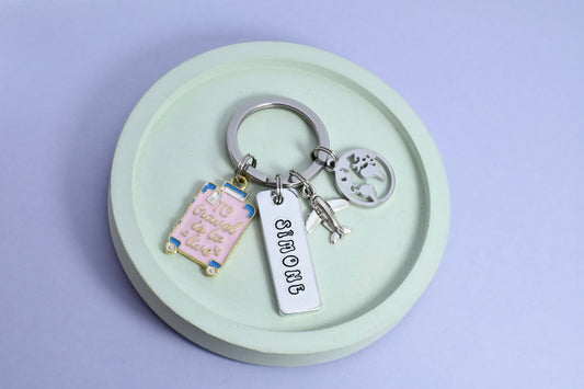 A personalised aluminium keyring with rectangular dimensions, featuring travel-themed charms including a plane, world, suitcase, and a split ring. 
