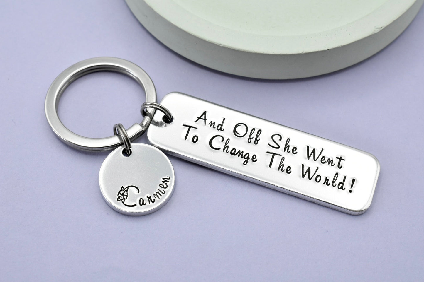 Silver aluminium keyring, larger rectangle says "And off she went to change the world!". Silver disc charm is personalised with a name.