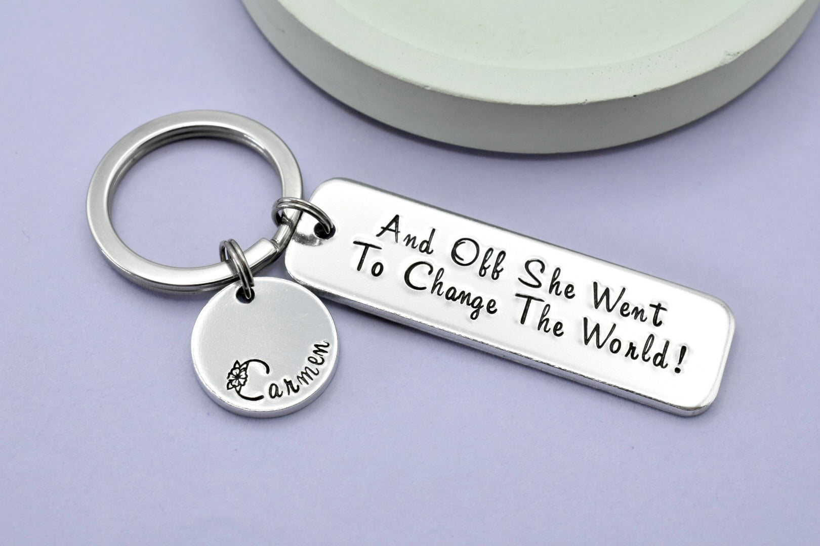 Silver aluminium keyring, larger rectangle says "And off she went to change the world!". Silver disc charm is personalised with a name.
