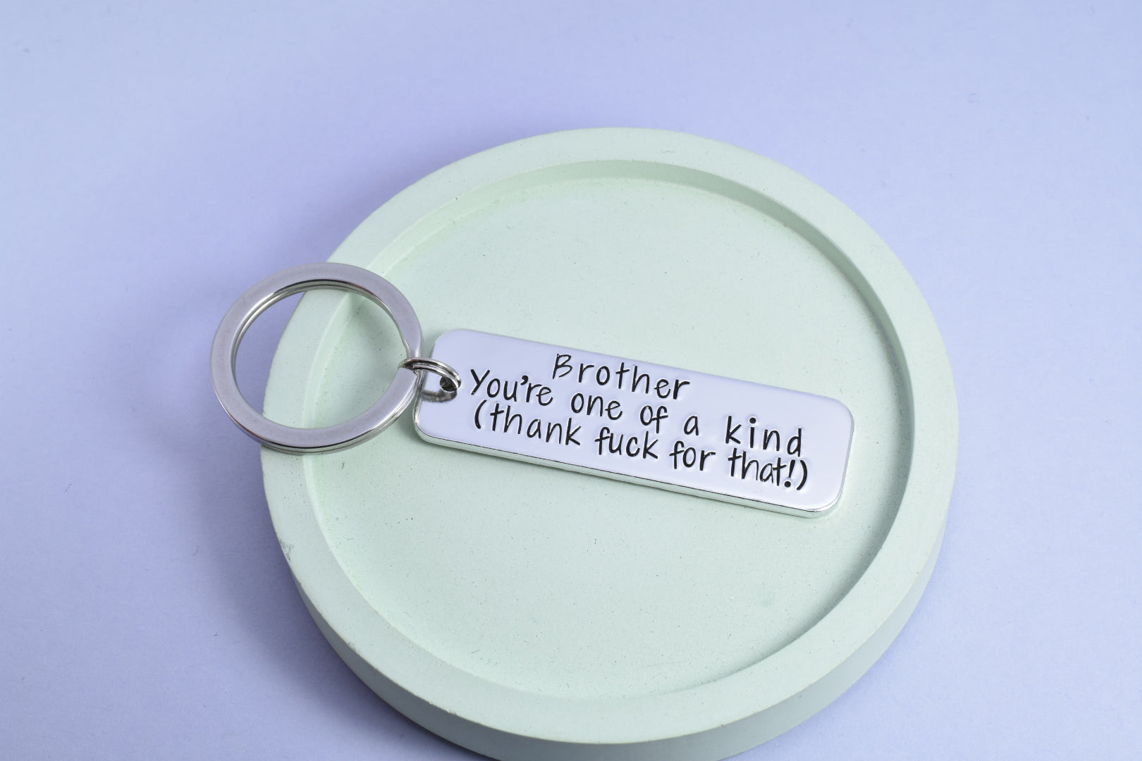 A rectangular keyring with the inscription 'Brother You're One Of A Kind, Thank Fuck For That' on it, attached to a split ring.
