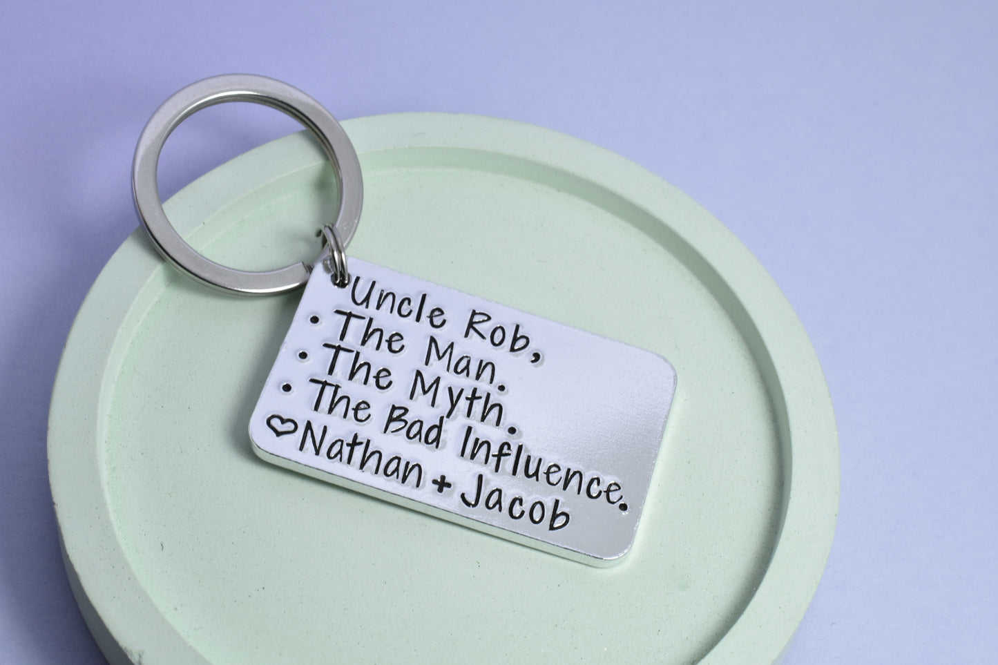 A personalised keyring with the text 'Uncle Rob, The Man, The Myth, The Bad Influence - Nathan & Jacob' hand stamped on a rectangular aluminum tag, attached to a keychain ring.