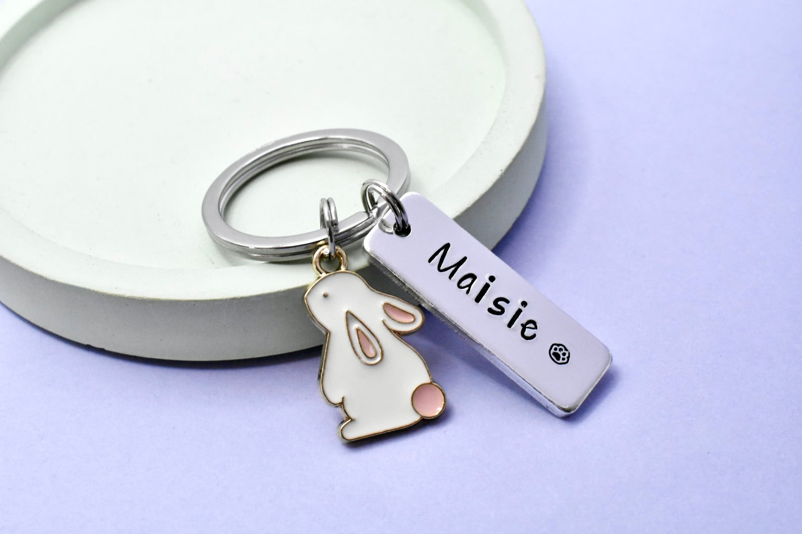 Keyring with white rabbit charm and personalised 'Maisie' tag on a light purple background