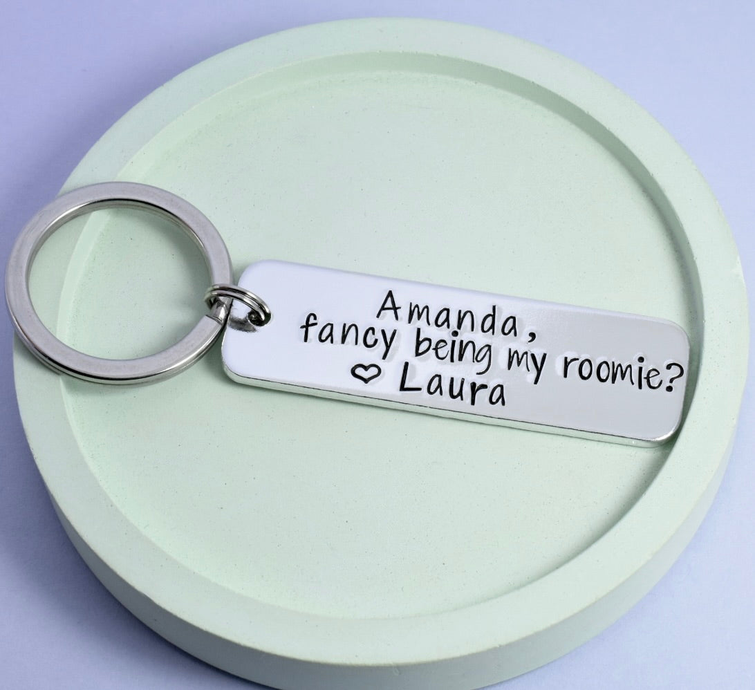 A personalised keyring, text reads "Amanda, facy being my roomie? heart design Laura"