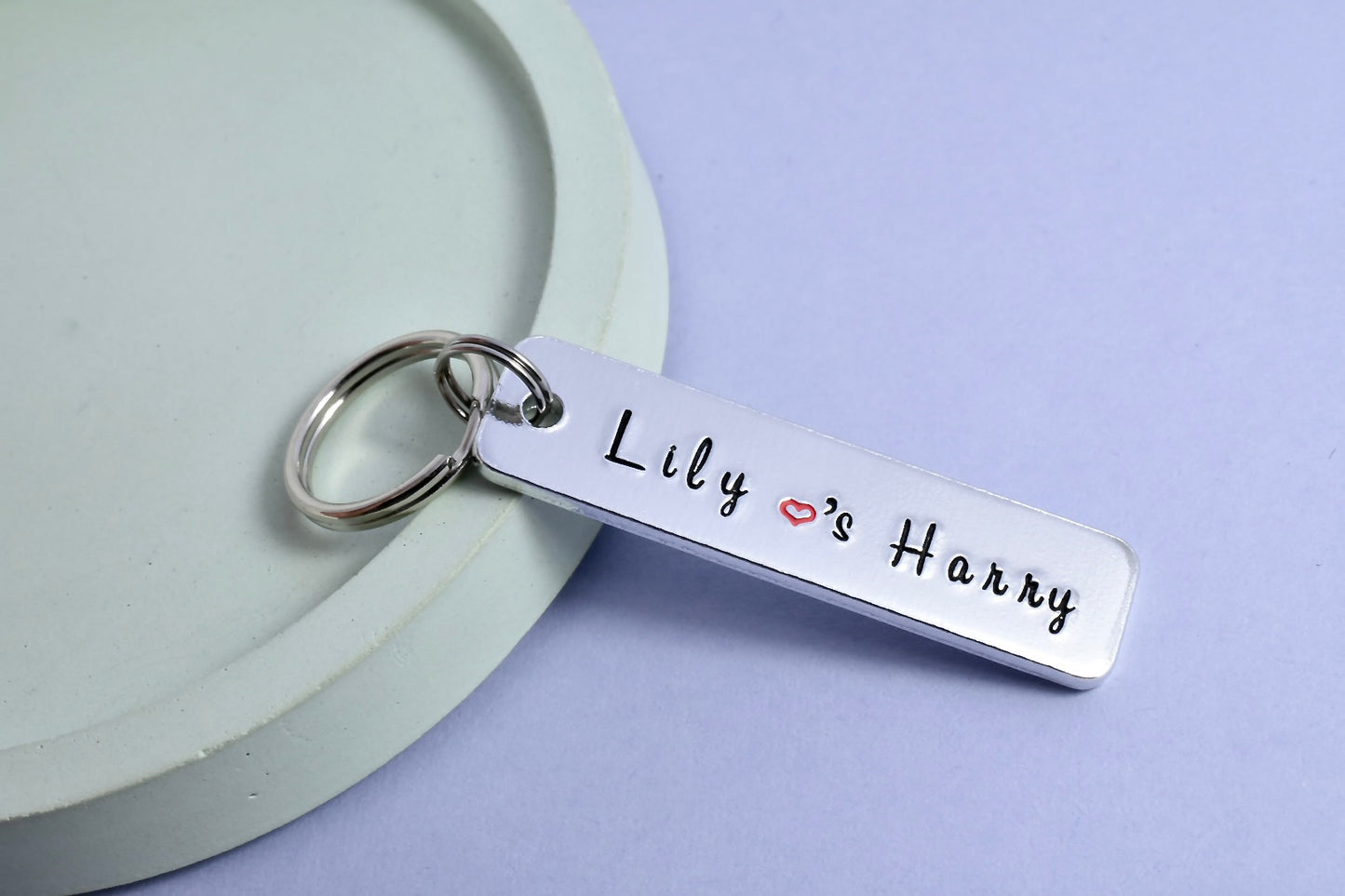 A personalised keyring with two names 'Lily & Harry', name's seperated by a small red heart, stamped on a rectangle shaped tag attached to a metal split ring.