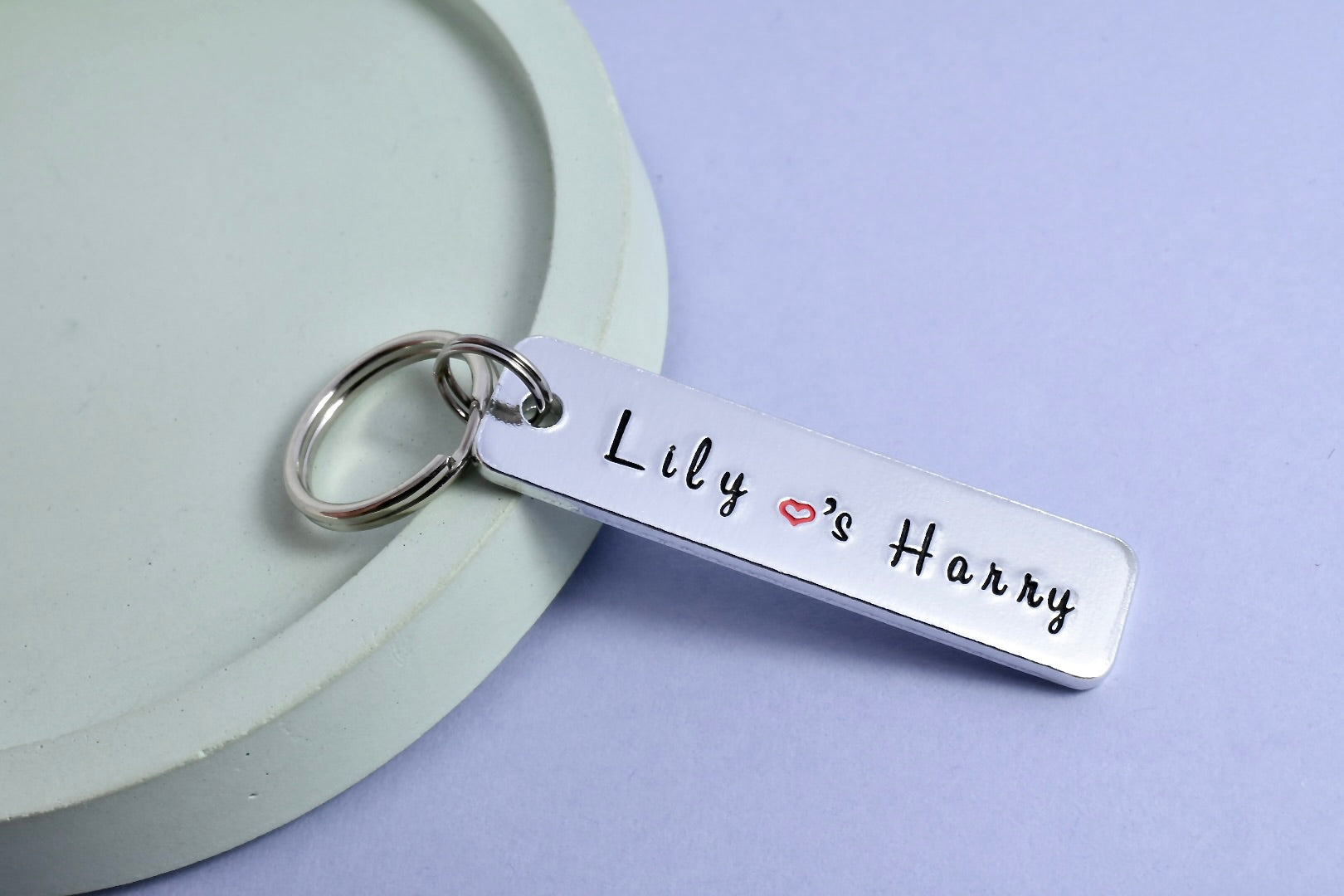 A personalised keyring with two names 'Lily & Harry', name's seperated by a small red heart, stamped on a rectangle shaped tag attached to a metal split ring.