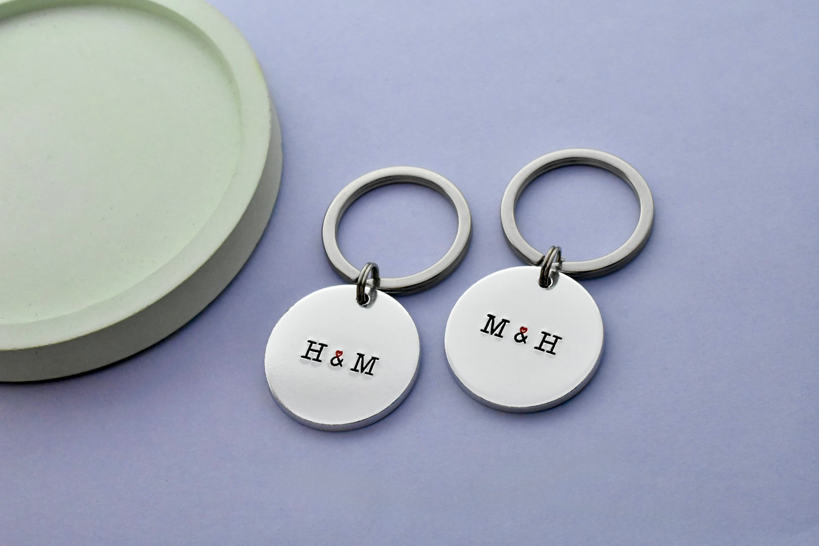 Two silver keychains with 'H & M' initials on a purple background