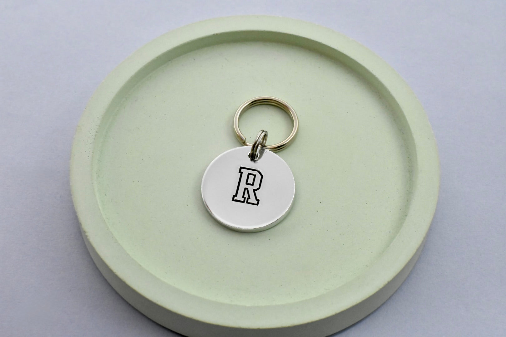 Small aluminium disc, hand stamped with a black initial on a small keyring