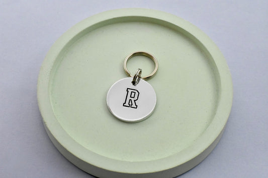 Small aluminium disc, hand stamped with a black initial on a small keyring