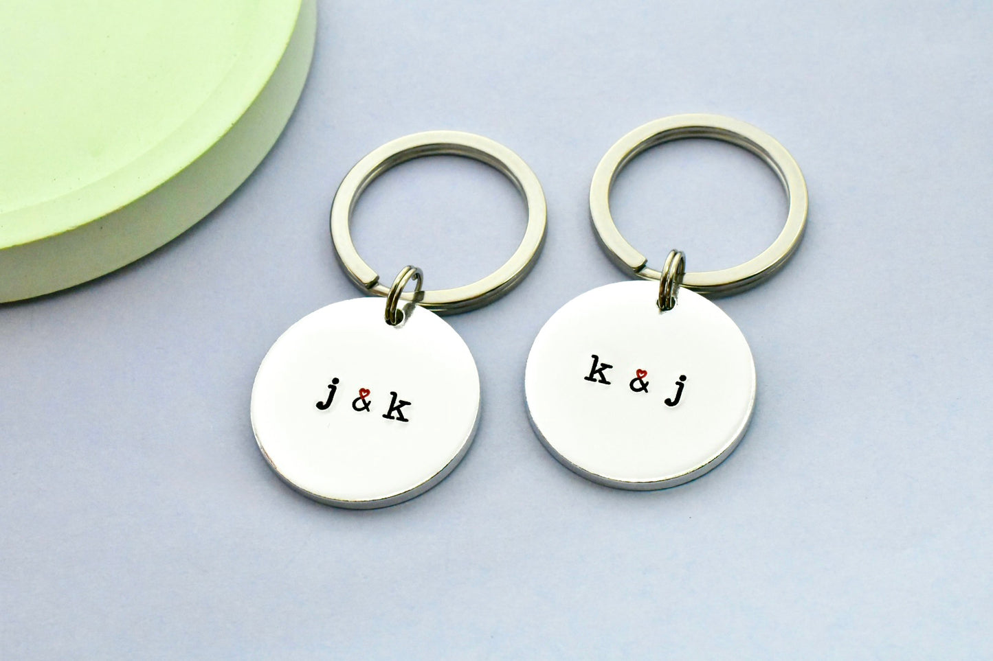 Pair of keyrings, made of aluminium, has initials on t that are separated by a heart ampersand