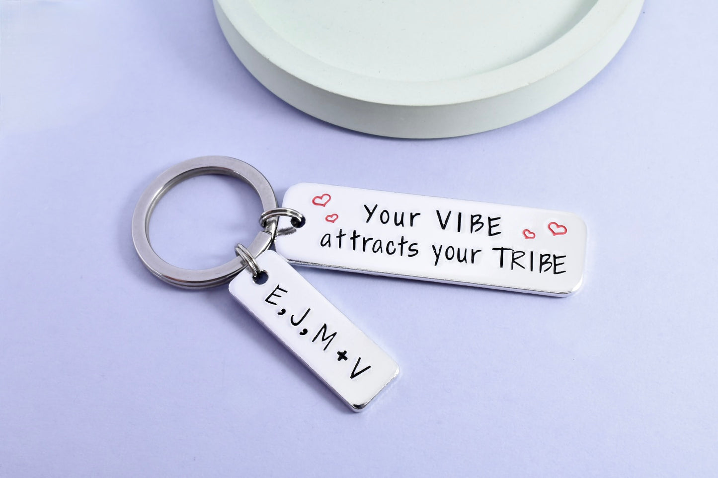 A silver keyring with a rectangular tag personalised with the message 'Your VIBE attracts your TRIBE' Smaller rectangle tag is personlised with friendship groups initials. The tag has a shiny surface with stamped hearts and initials.