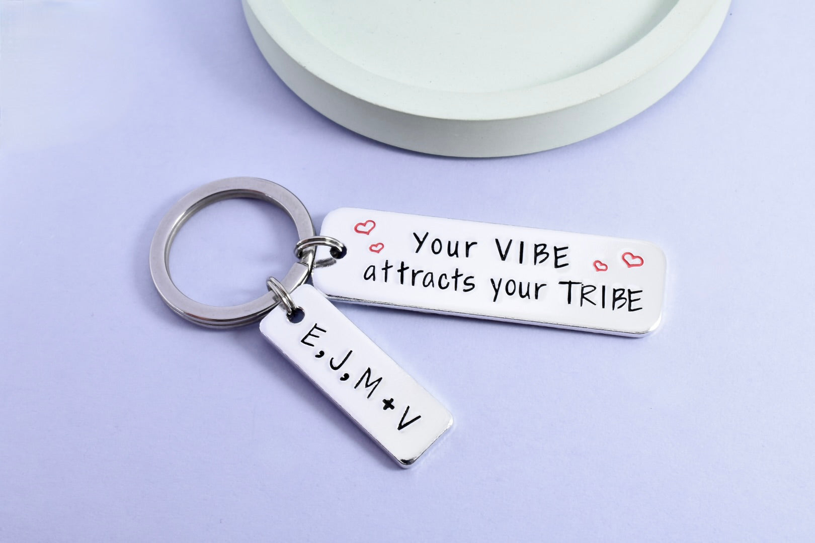 A silver keyring with a rectangular tag personalised with the message 'Your VIBE attracts your TRIBE' Smaller rectangle tag is personlised with friendship groups initials. The tag has a shiny surface with stamped hearts and initials.