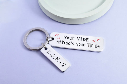 A silver keyring with a rectangular tag personalised with the message 'Your VIBE attracts your TRIBE' Smaller rectangle tag is personlised with friendship groups initials. The tag has a shiny surface with stamped hearts and initials.