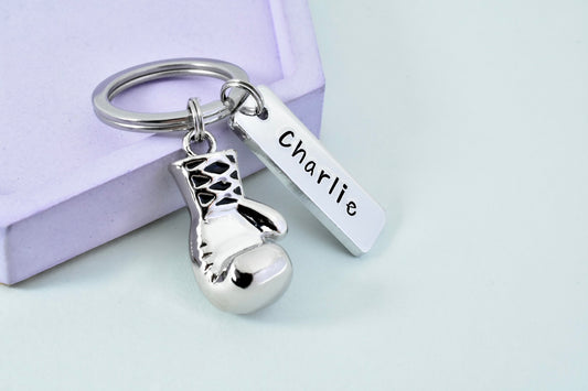 A personalised aluminium keyring with a 3D boxing glove charm and a rectangular tag that has the name 'Charlie' printed on it
