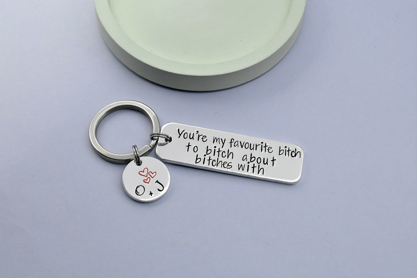 A silver-coloured keyring with a personalised inscription that reads 'You're my favourite bitch to bitch about bitches with', attached is also a small disc personalsied with friend's initials and trio of red heart design