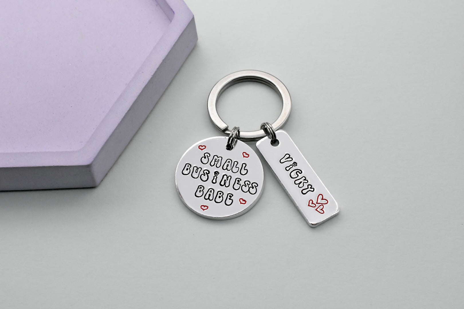 Silver aluminium keyring. Stmped with "Small Business Babe" and red hearts on disc and aluminium rectangle tag is personlaised with name and trio of red heart design, both are attached to a silver split ring.