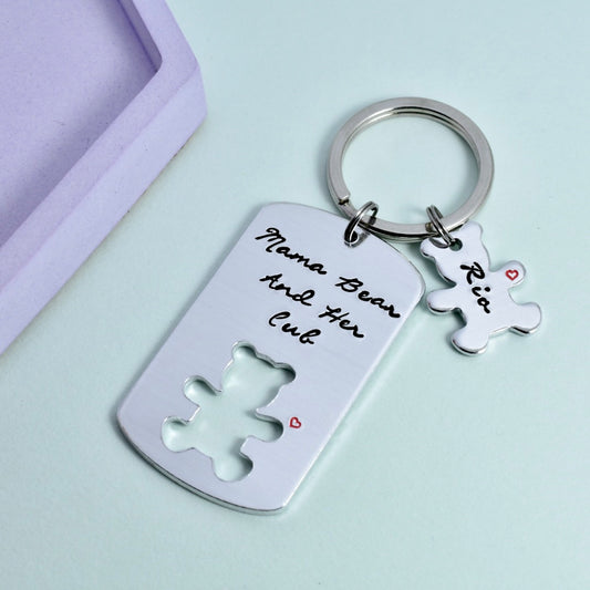 A personalised keyring with a bear and her cub design, with the inscription 'MAMA BEAR AND HER CUB' on a silver-colored ring. There is a small bear-shaped name charm attached to the ring.