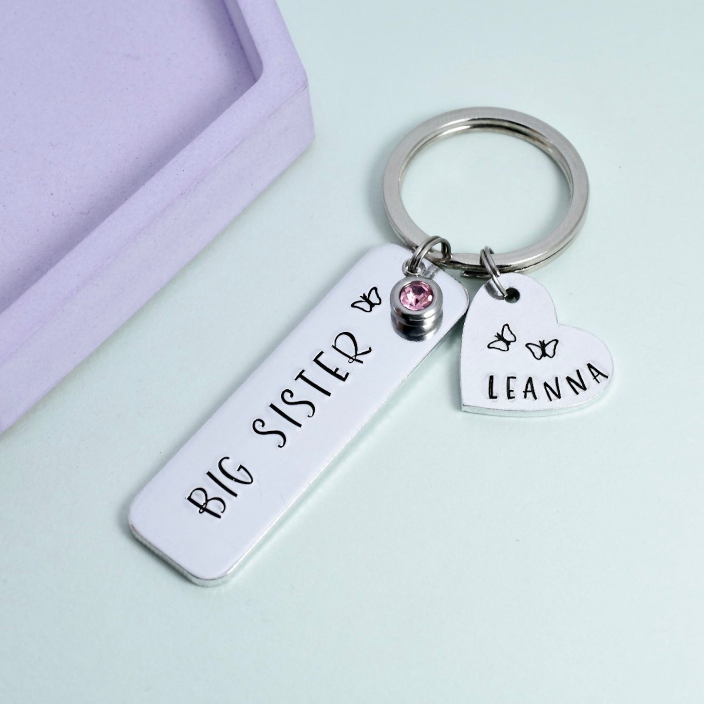 Silver aluminium rectangle keyring. big sister on rectangle with butterfly design and optional crystal charm. small heart charm is personalised with name and butterfly designs