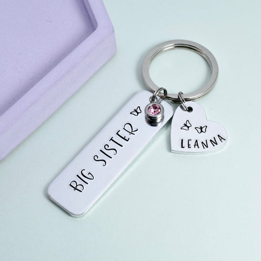 Silver aluminium rectangle keyring. big sister on rectangle with butterfly design and optional crystal charm. small heart charm is personalised with name and butterfly designs