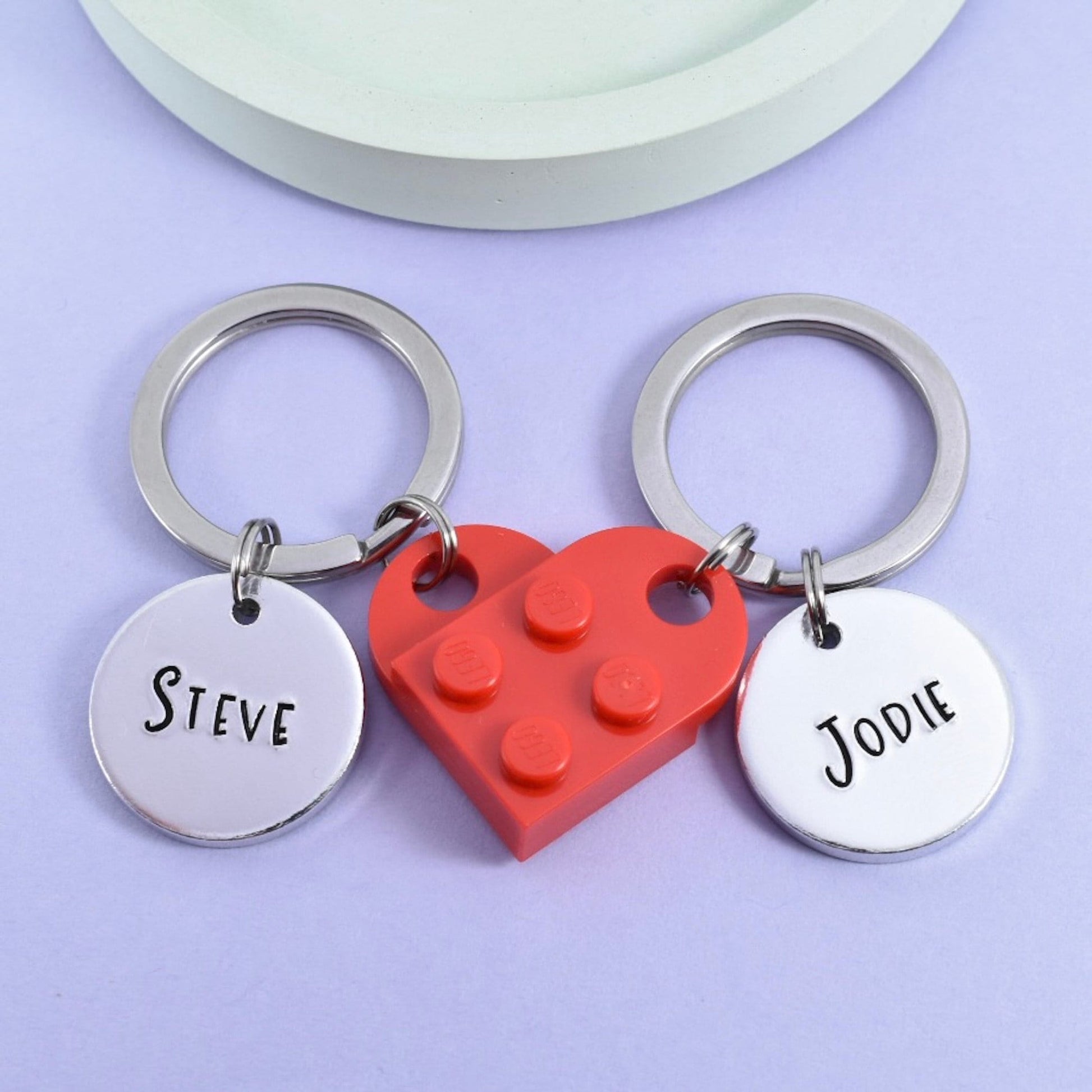 A set of two personalised keyrings made of plastic building blocks that when clicked together make a heart shape, each silver disc is customised with a name 'Steve' and 'Jodie' 