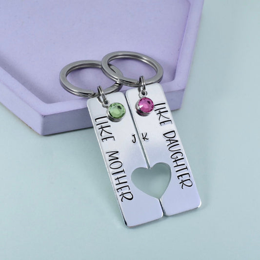 A set of two personalised keyrings with 'Like Mother, Like Daughter' inscribed on each, alongside crystal embellishments. Each keyring has a heart-shaped cut-out in the center.