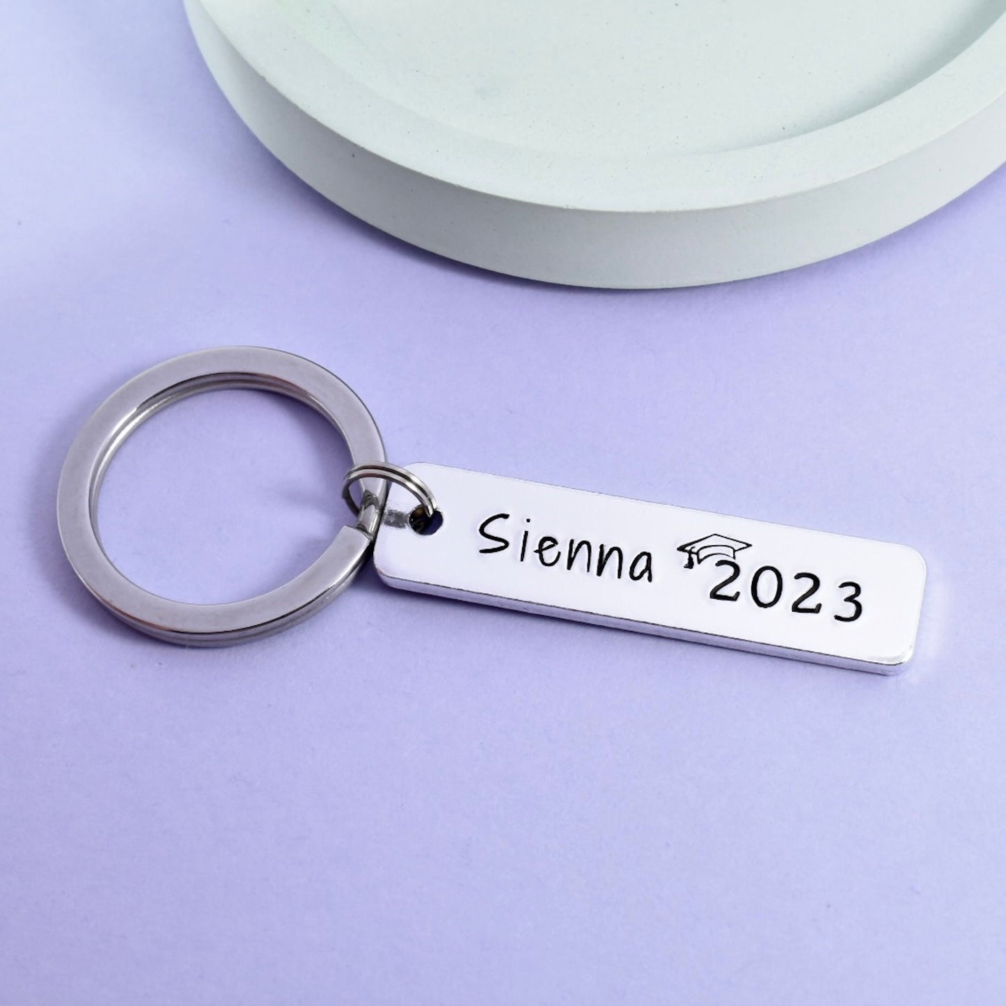 Graduation keyring. silver in colour and featuring a name and graduation year wearing a mortarboard hat