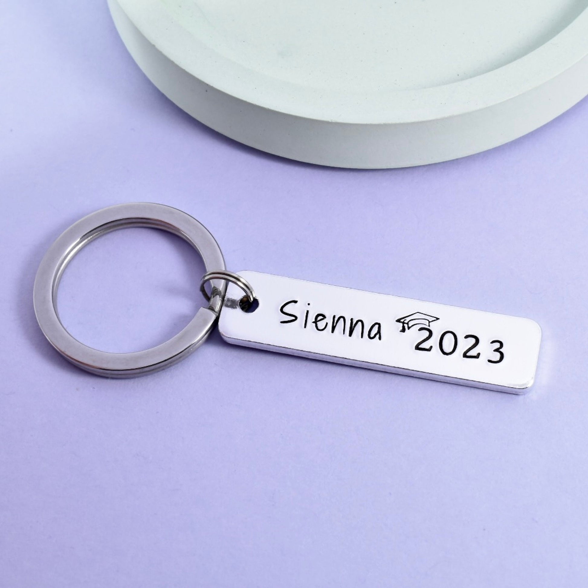 Graduation keyring. silver in colour and featuring a name and graduation year wearing a mortarboard hat