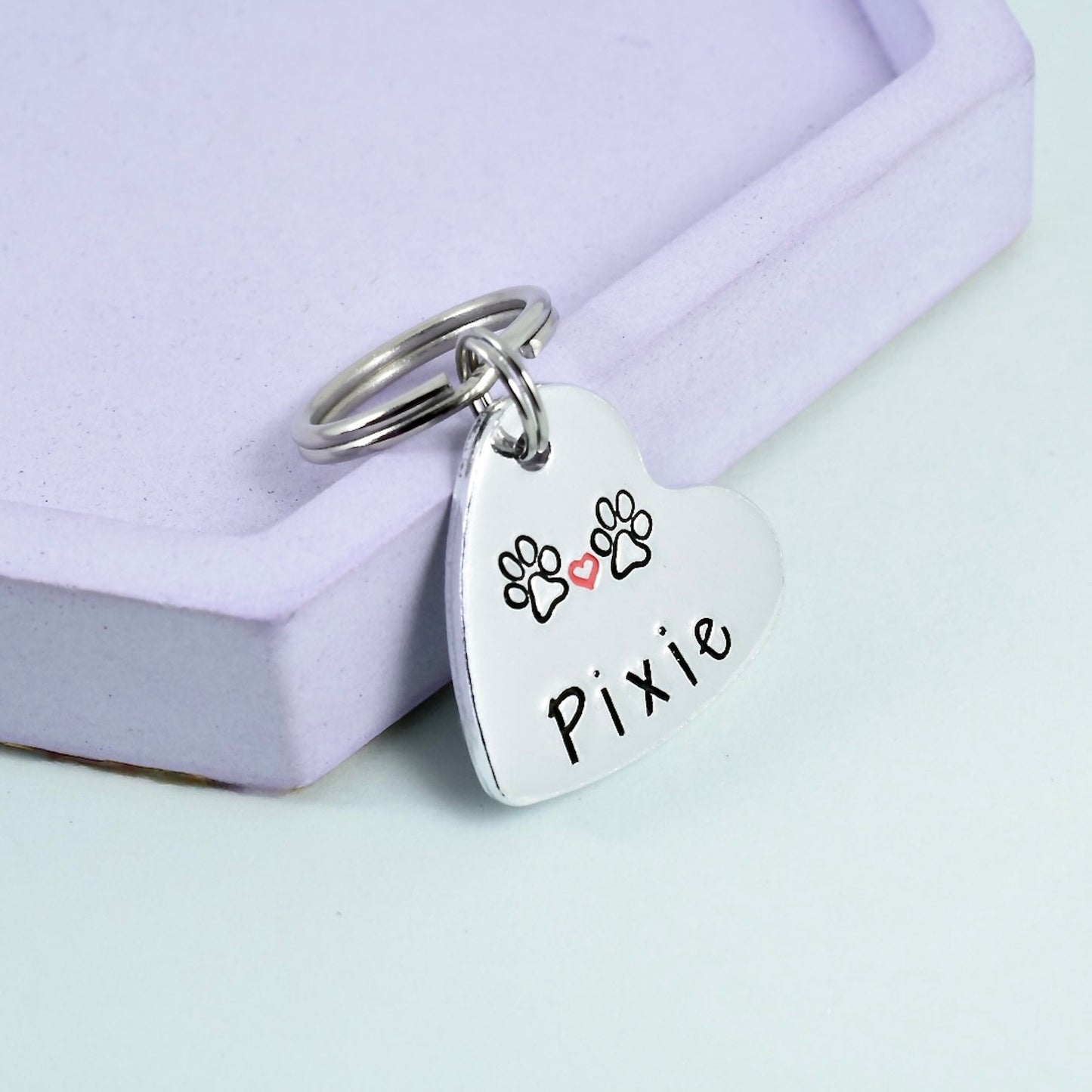 A personalised key ring with a heart-shaped aluminum tag that can be engraved, with the name 'Pixie' on it, with two pawrpint designs and small red heart 