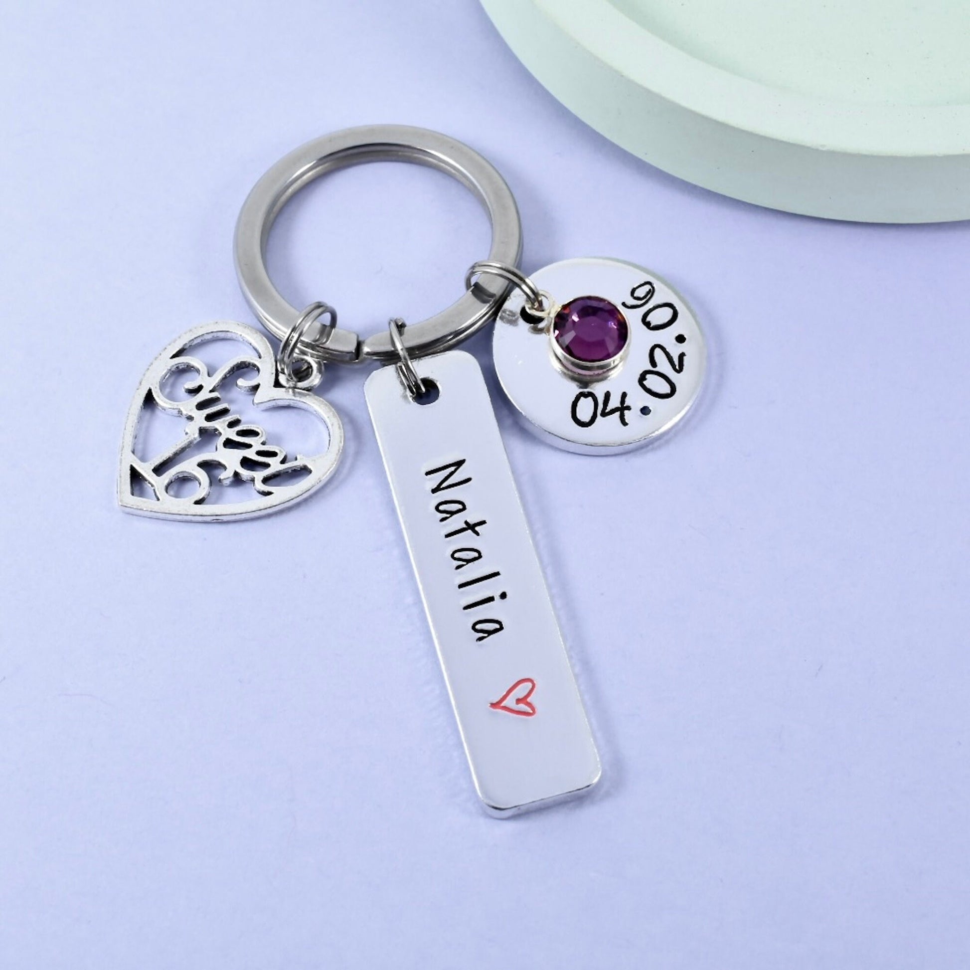 A personalised birthday keyring with a heart-shaped tag, a disc with the birth date, and a small crystal heart charm. Sweet 16th charm