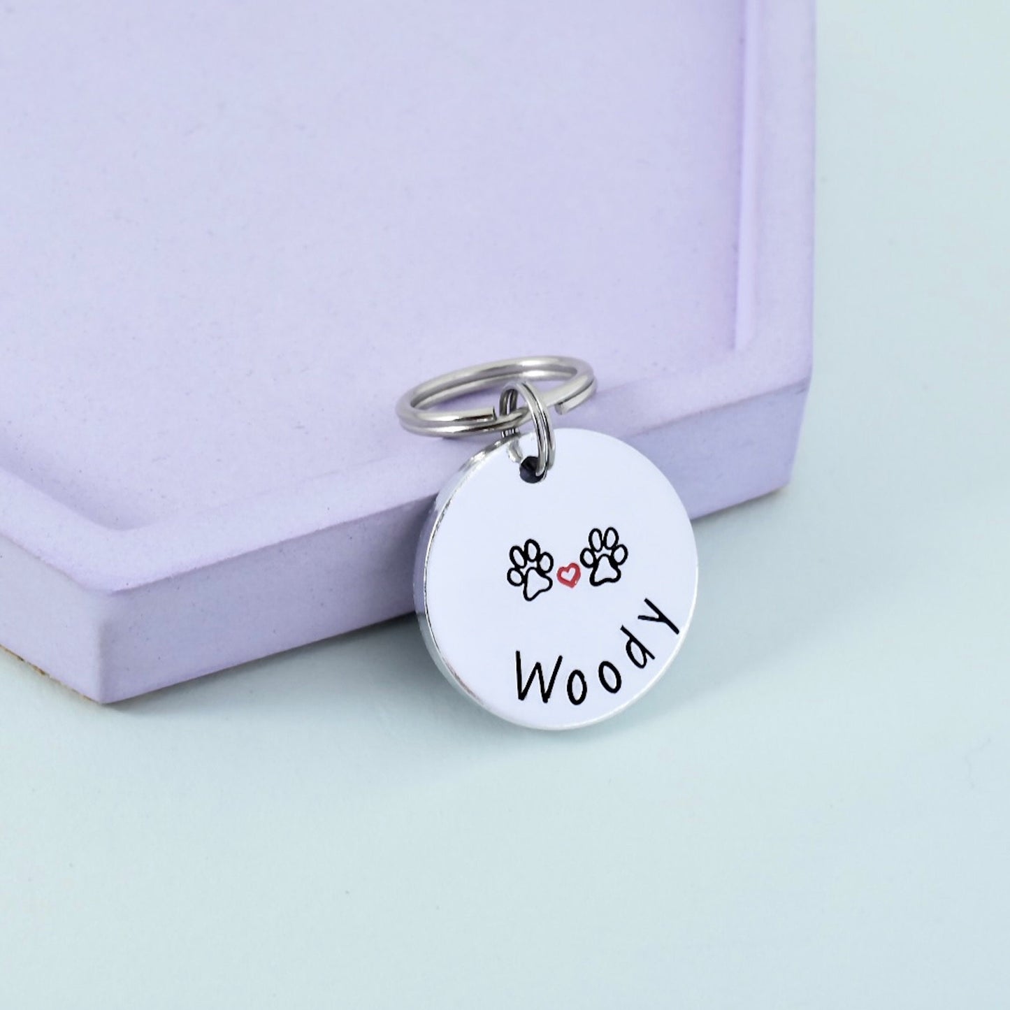 A personalized key ring with a metal disc tag that has the name 'Woody' and pawprint designs