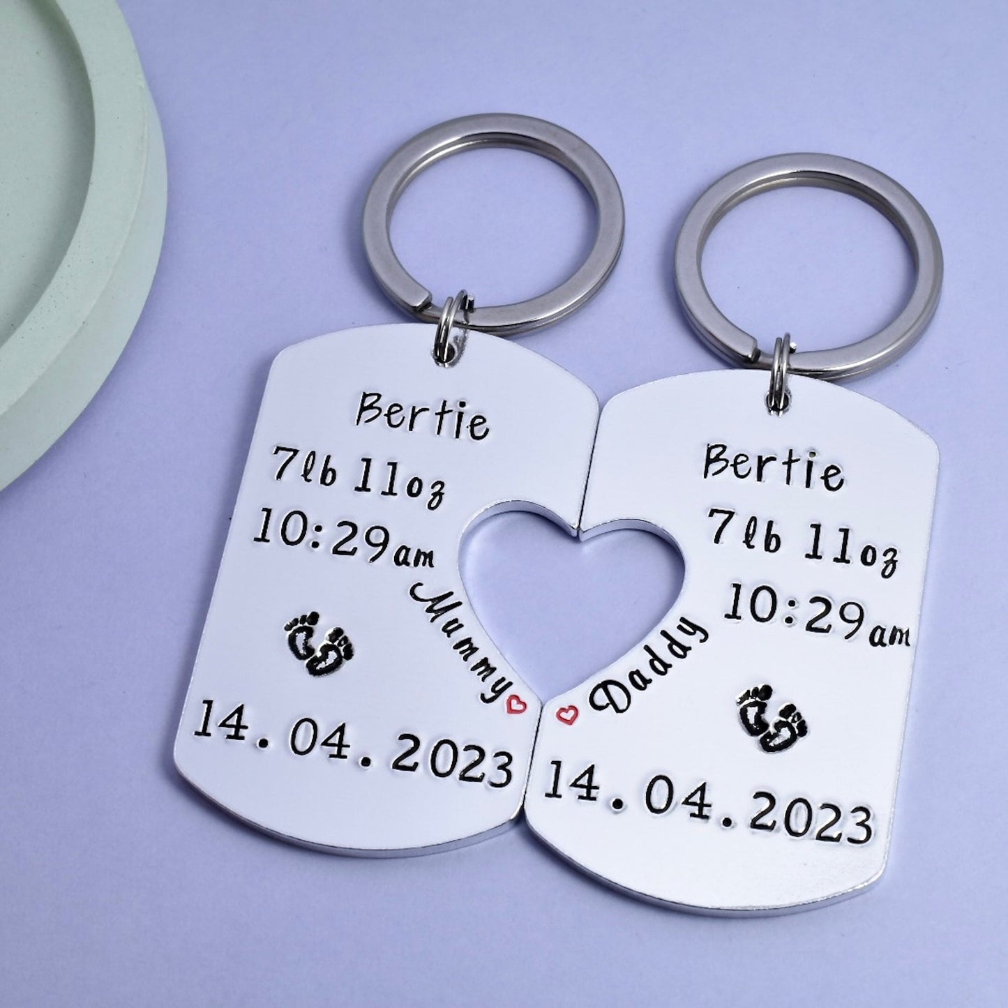 Two aluminium keyrings with personaliSed engravings of birth details, one with 'Mummy' and heart cut-out, the other with 'Daddy' and footprint stamp