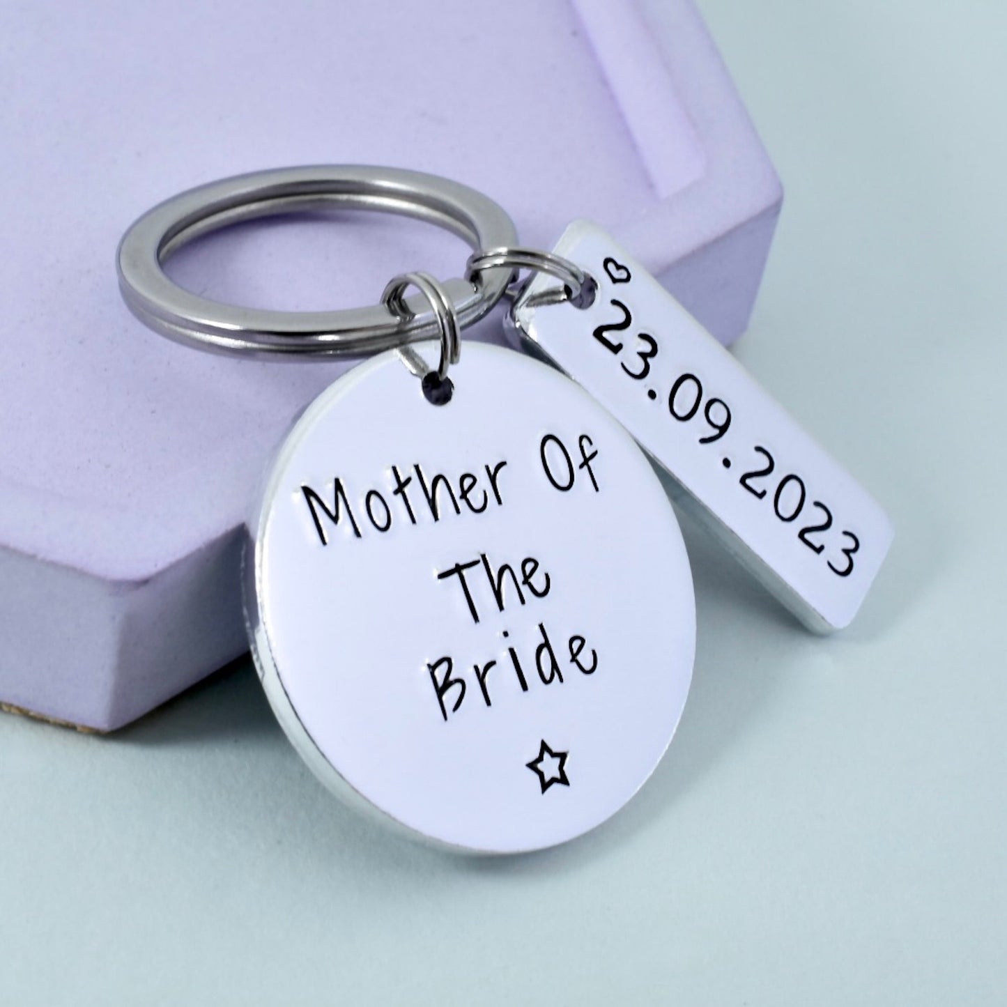 A personalised keyring with an aluminium disc stamped with 'Mother of the Bride' and a date, attached to a silver aluminium bar.