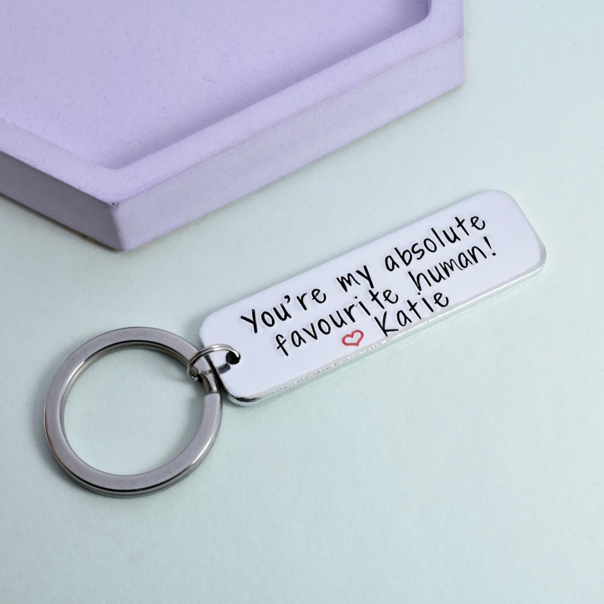 A personalised keyring with a rectangular tag, on which the message 'You're my absolute favourite human! - Katie' is stamped. 
