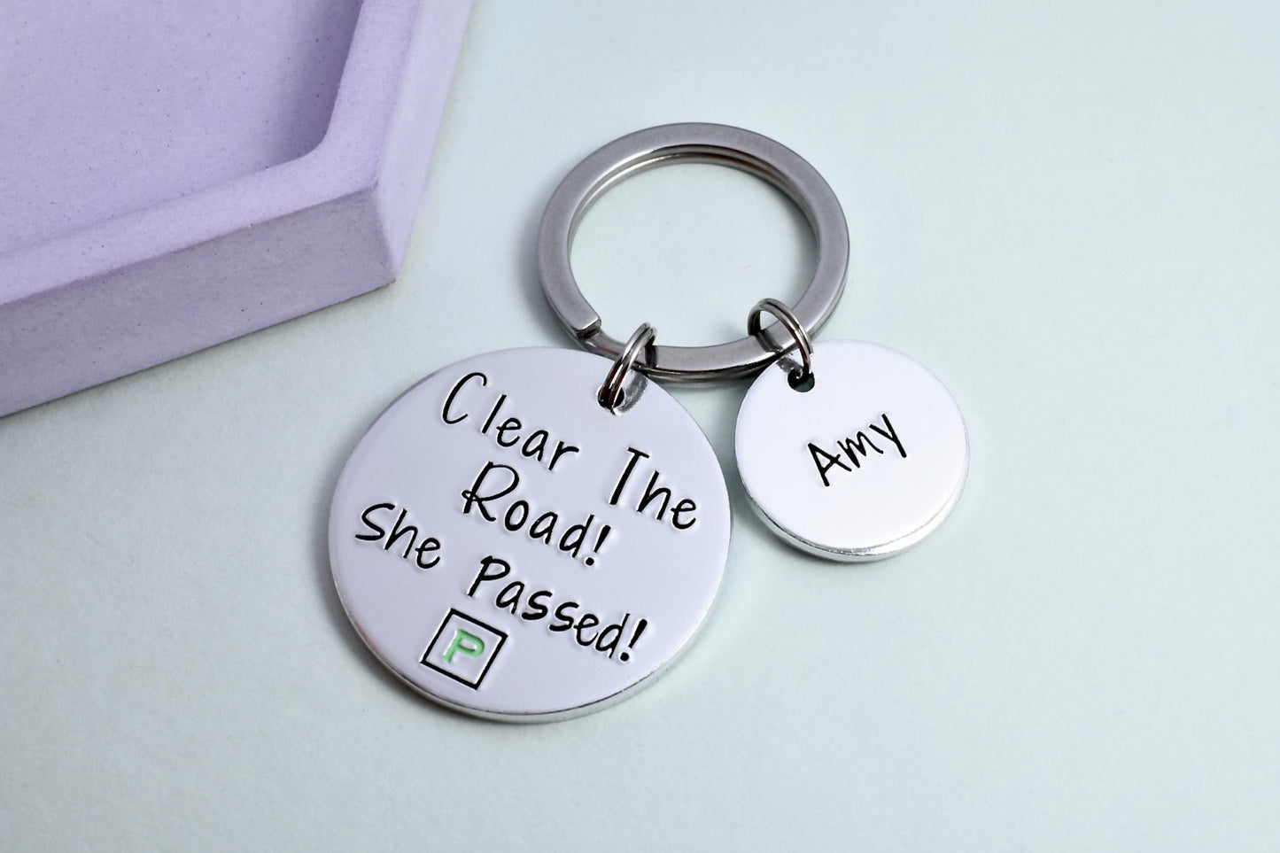 A personalised keyring with two aluminium discs, one large with the message 'Clear The Road! She Passed!' and a mock green P-Plate design, and one smaller with a personalisation of a name.
