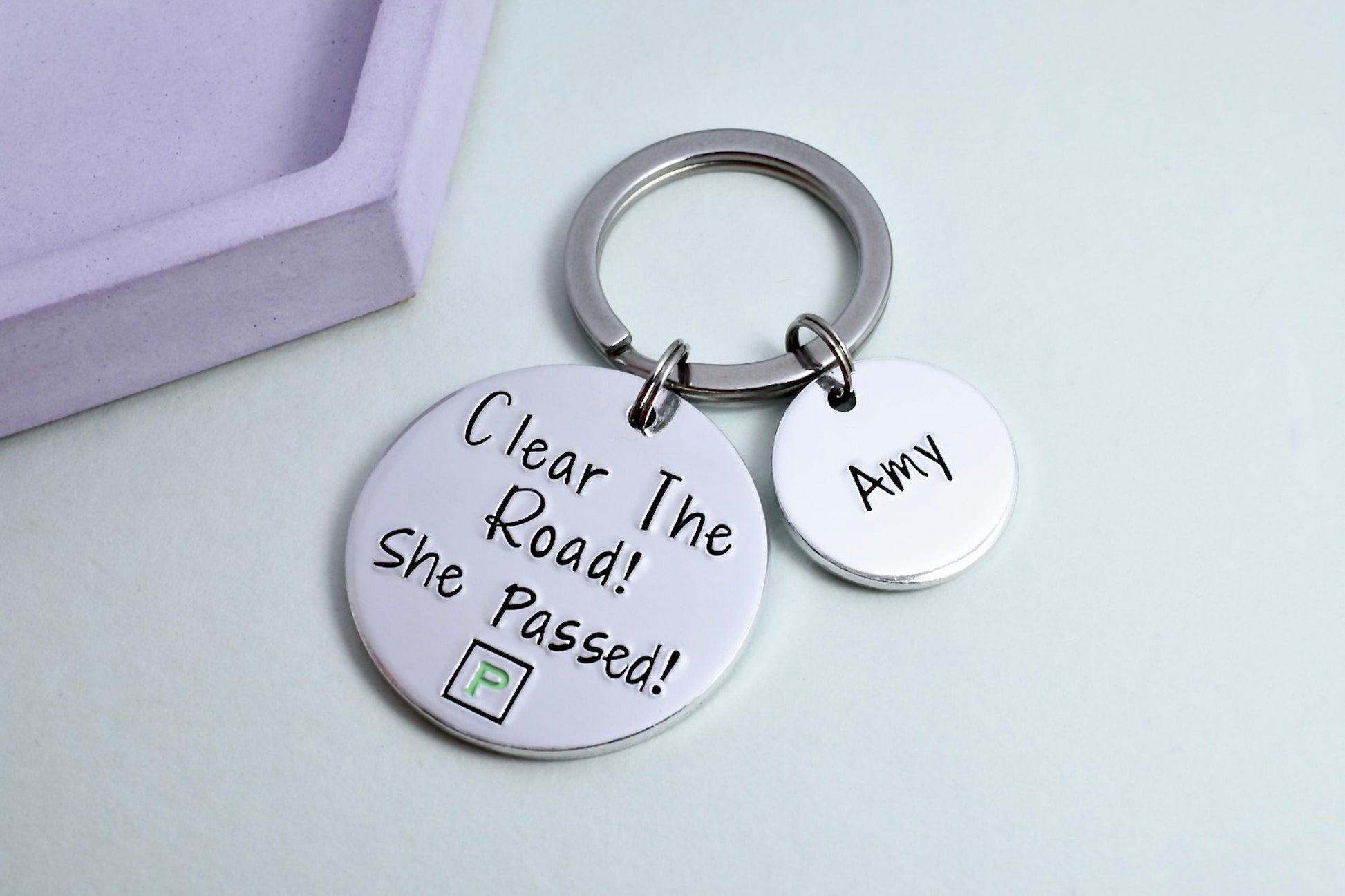 A personalised keyring with two aluminium discs, one large with the message 'Clear The Road! She Passed!' and a mock green P-Plate design, and one smaller with a personalisation of a name.
