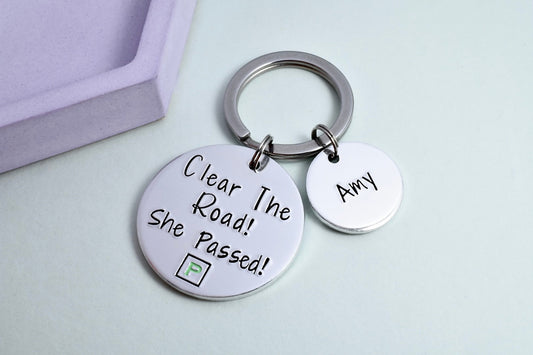 A personalised keyring with two aluminium discs, one large with the message 'Clear The Road! She Passed!' and a mock green P-Plate design, and one smaller with a personalisation of a name.