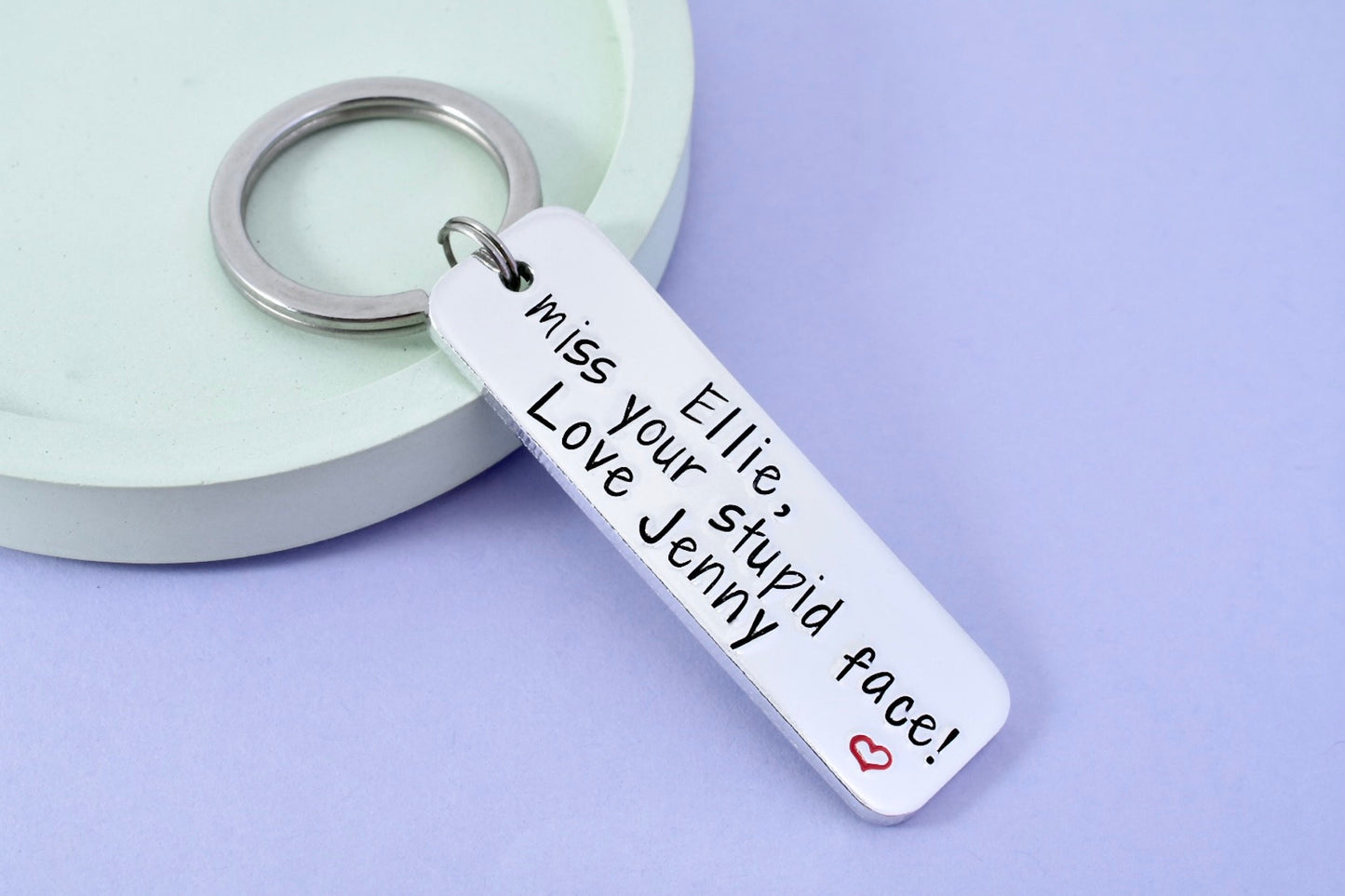 A silver keyring with a personalised message that reads 'miss your stupid face' attached to a card with the name 'Ellie'.