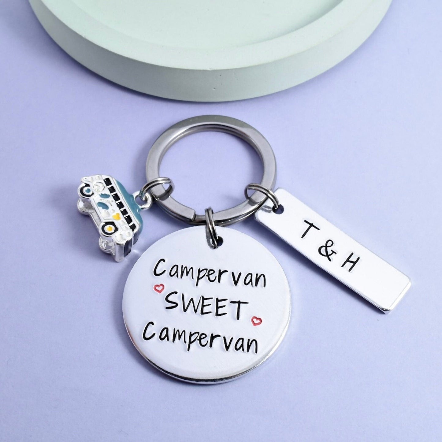A keyring with a round aluminium disc stamped with 'Campervan Sweet Campervan' and an aluminium rectangle tag with the initials 'T & H'. Also includes a small campervan charm and a split ring.